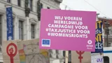 Demonstratie met een bord waarop staat: Wij voeren wereldwijd campagne voor #taxjustice voor #womensrights.