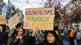 Vrouw in protestmars houdt bord omhoog met daarop de tekst: Kolonialisme verwoest de planeet