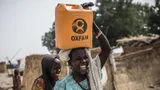 Een man draagt een jerrycan op zijn hoofd met het Oxfam logo.