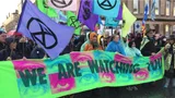 Demonstratie van XR Extinction Rebellion in Glasgow. Voorop is een spandoek met de tekst: We are watching you.