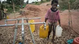Een Congolees jongetje loopt met twee jerrycans bij een waterpunt.
