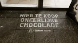 Green graffiti voor een supermarktdeur waarop 'Hier te koop oneerlijk chocolade'