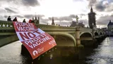 Activisten laten een spandoek over een brug hangen met de tekst: People's vaccine, not profit vaccine.