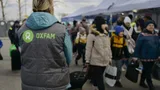 Vluchtelingen aan de grens, onderweg met hun spullen, samen met een Oxfam-medewerker vanaf de rug gezien.