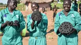 Photograph of three people holding circular objects with holes drilled into the objects
