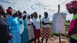 African women listen to a woman showing them something on a large piece of paper.
