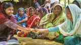 A group of women in India. One hands a banknote to another woman.