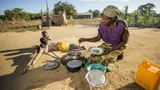 Een vrouw in Mozambique maakt ondanks de droogte een beetje eten voor twee kinderen.