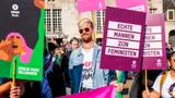 Een mannelijke Oxfam-medewerker staat met een bord 'Echte mannen zijn feministen"