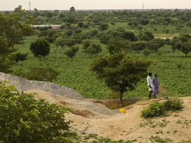 Twee mensen lopen door een groen landschap in Nigeria.