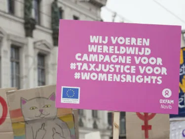 Demonstratie met een bord waarop staat: Wij voeren wereldwijd campagne voor #taxjustice voor #womensrights.