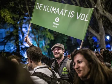 Foto van man die tijdens een klimaatpotest een spandoek omhooghoudt met de tekst De Klimaat is Vol