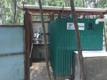 Een toiletgebouw van golfplaten met de logo's van UNICEF en Oxfam.
