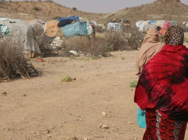 Twee vrouwen op de rug gezien die lopen naar een tentenkamp in een droog landschap.