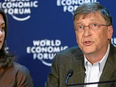 Bill Gates spreekt op het World Economic Forum. Naast hem kijkt een vrouw toe.