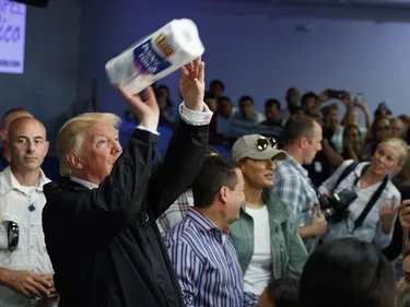 President Trump gooit wc rollen. Naast hem staat een groep mensen.