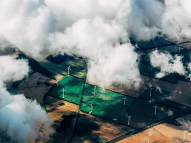Foto vanuit de lucht van wolken boven weilanden met windmolens.