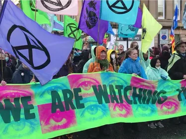 Demonstratie van XR Extinction Rebellion in Glasgow. Voorop is een spandoek met de tekst: We are watching you.