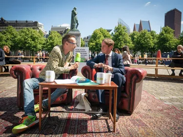 Dolf Jansen zit buiten op het Plein in Den Haag op een bank naast Kamerlid Nijboer (PvdA) en interviewt hem.