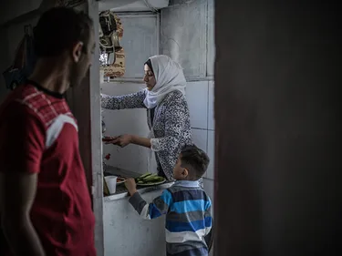 Fatem werkt in de keuken. Haar man en haar zoontje Mohammed kijken toe.