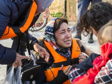 Huilende vrouw met reddingsvest aan wordt opgevangen in Griekenland.