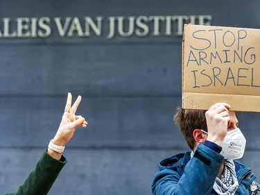 Actievoerder houdt bij het Paleis van Justitie een bord omhoog met de tekst: Stop arming Israel