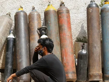 Een man met een mondkapje zit voor een muur waartegen gasflessen staan.