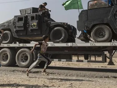 Kinderen zwaaien naar gevechtsvoertuigen van het Iraakse leger, onderweg naar Mosul.