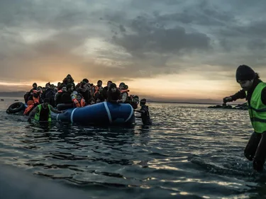 Een rubberboot vol mensen wordt door iemand met een touw naar de kant getrokken.