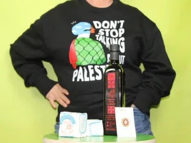 Een persoon met een zwarte trui met tekst "don't stop talking about palestine", olijfolie, zeep en een pin met illustratie van Xaviera Altena.
