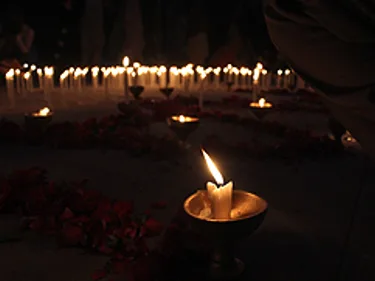 Een brandende kaars staat voor een rij andere brandende kaarsen.