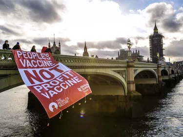 Activisten laten een spandoek over een brug hangen met de tekst: People's vaccine, not profit vaccine.