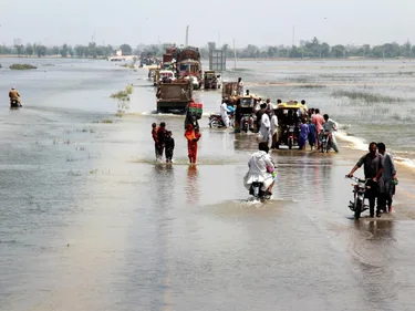 Foto van mensen die een overstroomde snelweg oversteken in het Dadu-district, provincie Sindh, Pakistan.