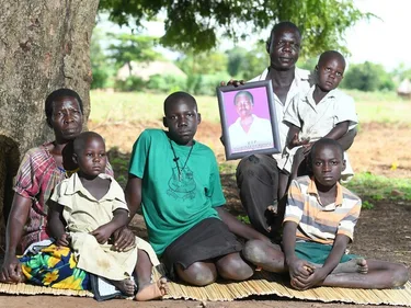 Op de foto (vlnr): Buurvrouw Margret, die helpt met de tweeling Apio Stella Rose en Acen Florance Jannet (beiden op schoot), vader Ogwang James met het portret van zijn overleden vrouw Akol Stella Rose, hun dochter Asio Everlyn en zoon Ogwang Brain.