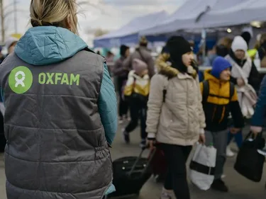 Vluchtelingen aan de grens, onderweg met hun spullen, samen met een Oxfam-medewerker vanaf de rug gezien.