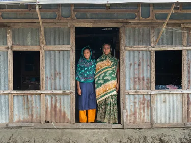 Twee vrouwen in Bangladesh staan in de deuropening van hun huis. Door klimaatverandering hebben ze steeds meer last van overstromingen.