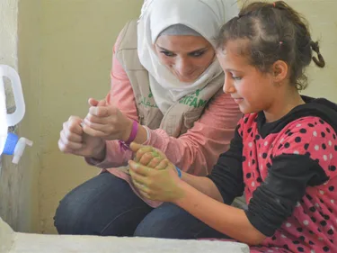 Foto van vrijwilliger in Syrië die aan kind laat zien hoe je je handen wast.