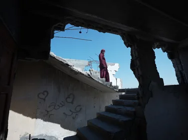 Een Palestijnse vrouw staat tussen gebombardeerde huizen in Gaza.