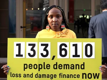Elizabeth Wathuiti with a sign saying: 133,610 people demand loss and damage finance now.