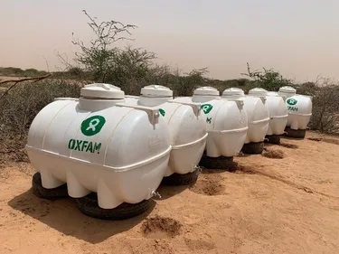 Watertanks met het Oxfam logo op een zandvlakte.