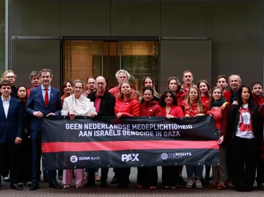 Advocaat Liesbeth Zegveld, Michiel Servaes, en andere Oxfam Novib-medewerkers poseren in het rood voor de Hoge Raad met een spanddoek met daarop de tekst: "Geen Nederlandse medeplichtigheid aan Israëls genocide in Gaza."