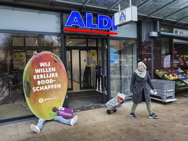 Een kartonnen protestbord in de vorm van een mango met daarop "wij willen eerlijke boodschappen" bij de ingang van de Aldi
