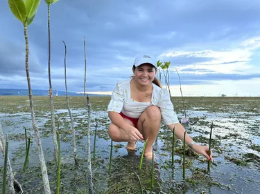 Activist Marinel hurkt naast jonge mangrovebomen die ze heeft geplant
