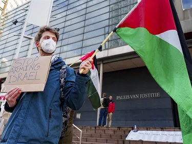 Man met een Palestijnse vlag en een bordje met 'Stop arming Israel' demonstreert voor het Paleis van Justitie