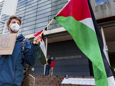 Man met een Palestijnse vlag en een bordje met 'Stop arming Israel' demonstreert voor het Paleis van Justitie