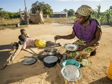 Een vrouw in Mozambique maakt ondanks de droogte een beetje eten voor twee kinderen.