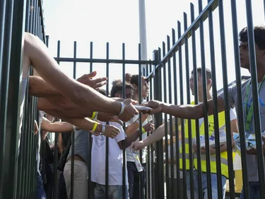 Foto van asielzoekers achter een hekwerk die hulpmiddelen uitgedeeld krijgen.