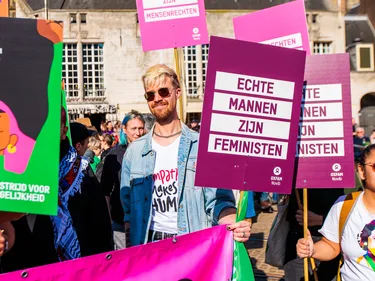 Een mannelijke Oxfam-medewerker staat met een bord 'Echte mannen zijn feministen"