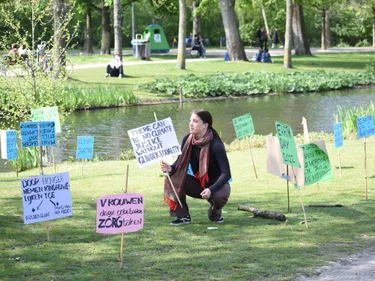 Een activist hurkt op het gras tussen protestborden