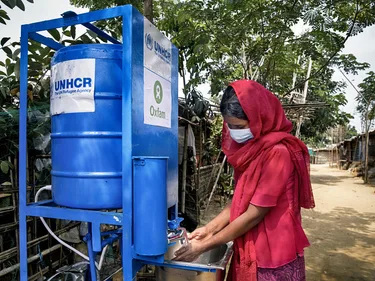 Een vrouw met mondkapje wast haar handen bij een Oxfam contactloos waterpunt